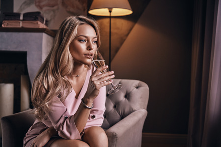 Just relaxing. Attractive young woman drinking champagne while sitting in the armchairの写真素材