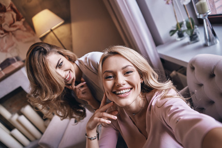 Flirty beauties.  Top view self portrait of attractive young women smiling and looking at camera while sitting on the sofaの写真素材