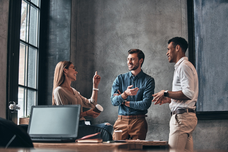 Discussing project together. Group of young confident business people discussing something and smiling while spending time in the officeの写真素材