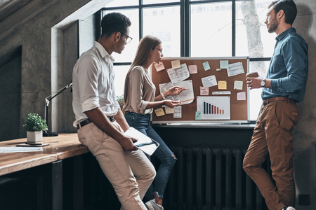 Passionate about their project. Three young business people using blackboard with adhesive notes while working in the officeの写真素材