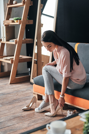 Perfect shoes. Thoughtful young woman trying on elegant shoes with high heels while sitting in the shoe storeの写真素材