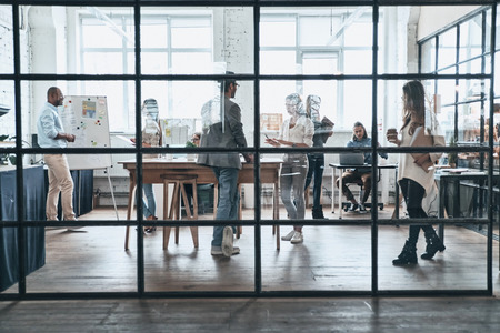 Successful professionals. Large group of young modern people working and communicating together while standing behind the glass wall in the board roomの写真素材