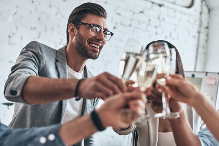 Well done everybody. Group of young business people toasting each other and smiling while standing in the board roomの写真素材