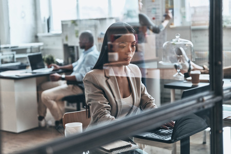Concentrated at work. Modern young woman using computer while working behind the glass wall in the officeの写真素材
