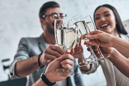 Colleagues and friends. Group of young business people toasting each other and smiling while standing in the board roomの写真素材