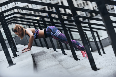Sport is the way of her life. Modern young woman in sport clothing keeping plank position while exercising on the steps outdoorsの写真素材