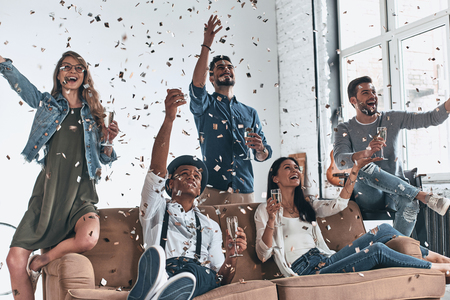Group of happy young people in casual wear drinking champagne while having a party with confetti flying everywhereの写真素材