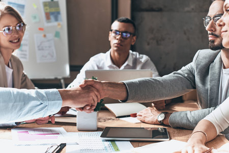 Young modern men in smart casual wear shaking hands while working in the creative office
