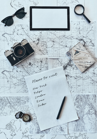 Planning vacation. High angle shot of sunglasses, photo camera, compass, magnifying glass, paper with written checklist and passport lying on mapの写真素材