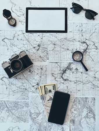 Just travel. High angle shot of sunglasses, photo camera, compass, magnifying glass, smart phone, passport and currency lying on mapの写真素材