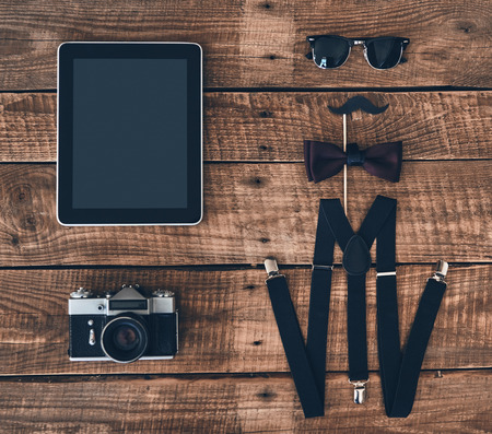 Modern elegance. High angle shot of digital tablet, photo camera, suspenders, prop, bow tie and eyewear lying on wooden deskの写真素材