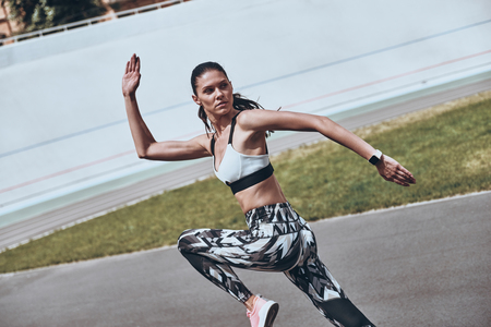 Making effort. Beautiful young woman in sports clothing running while exercising outdoorsの写真素材