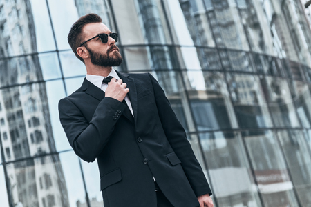 Confident and handsome. Good looking young man in full suit and sunglasses adjusting his necktie while standing outdoorsの写真素材
