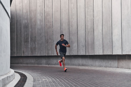 Morning workout. Full length of young man in sports clothing running while exercising outside