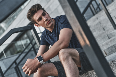Young athlete. Serious young man in sports clothing looking away while sitting outsideの写真素材