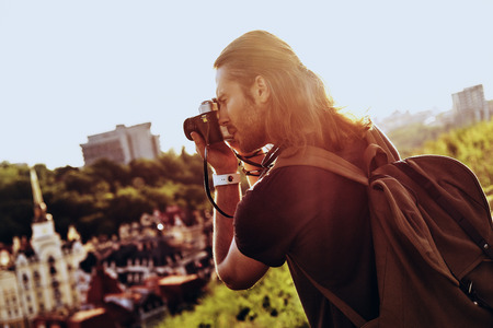 Nice shot. Young man in casual clothing photographing the view while standing on the hill outdoorsの写真素材