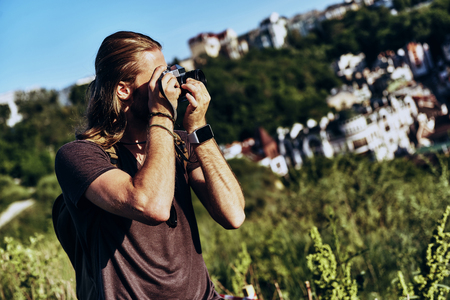 Great shot. Young man in casual clothing photographing the view while standing on the hill outdoorsの写真素材