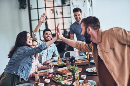 High-five! Young man and woman giving each other high-five while enjoying dinner party among friends