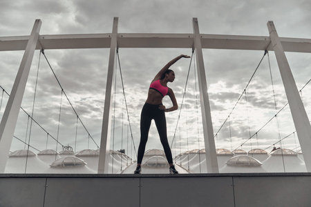 Energy inside. Full length of modern young woman in sports clothing stretching while warming up...