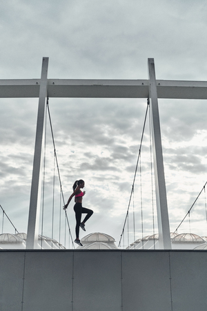 Exercising outdoor. Full length of modern young woman in sports clothing jumping while exercising outdoorsの写真素材