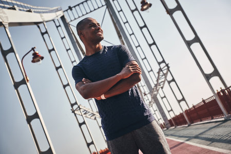 Healthy and happy. Handsome young African man in sports clothing smiling and looking away while standing on the bridge outdoorsの写真素材