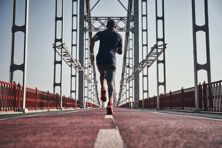 Never give up. Full length rear view of young African man in sports clothing exercising while jogging on the bridge outdoorsの写真素材