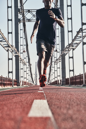 Morning workout. Close up of young African man in sports clothing exercising while jogging on the bridge outdoorsの写真素材
