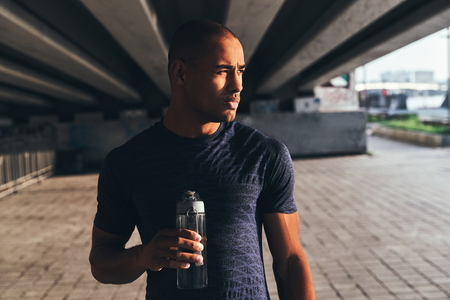 After workout. Young African man in sports clothing drinking water while standing outsideの写真素材