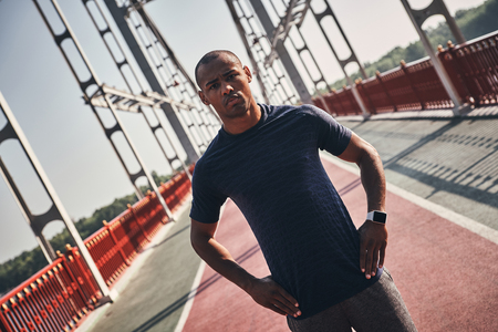 Strong athlete. Handsome young African man in sports clothing looking at camera while standing on the bridge outdoorsの写真素材