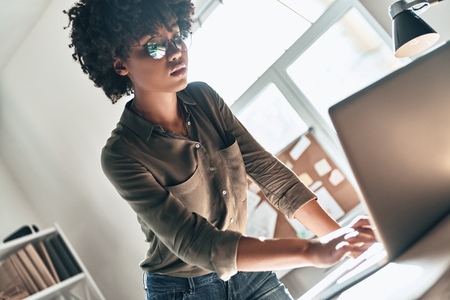 Young expert. Attractive young African woman using laptop while working in the officeの写真素材