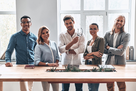 Happy business partners. Group of young modern people in smart casual wear looking at camera and smiling while standing in the creative officeの写真素材