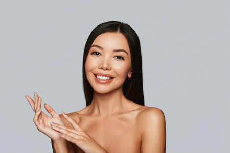 Feeling free and relaxed. Beautiful young Asian woman looking at camera and smiling while standing against grey backgroundの写真素材