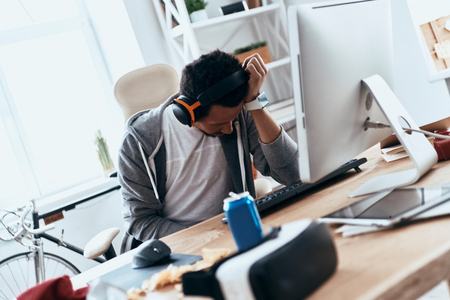 Failure. Frustrated young man in casual clothing leaning on his hand while spending time at homeの写真素材