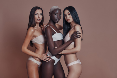 Effortless beauty. Three attractive mixed race women looking at camera while standing against brown backgroundの写真素材