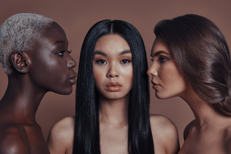 Gorgeous beauties. Three attractive young women looking at camera while standing against brown backgroundの写真素材