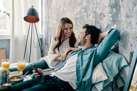 No cares. Beautiful young couple having breakfast while spending time in bed at homeの写真素材
