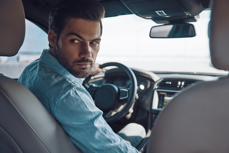 Ready to go? Rear view of young man in smart casual wear looking over shoulder while driving a status carの写真素材
