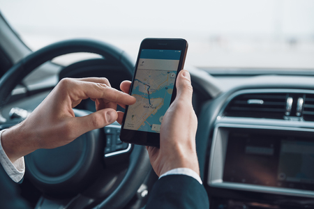 Checking the direction. Close up of young man using smart phone to check the map while driving a carの写真素材