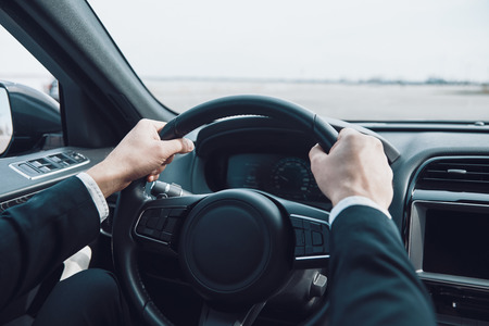 Drive carefully! Close up of man keeping hands on the steering wheel while driving a carの写真素材