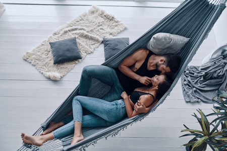 Loving everything about her. Top view of beautiful young couple embracing and smiling while resting in the hammock indoorsの写真素材