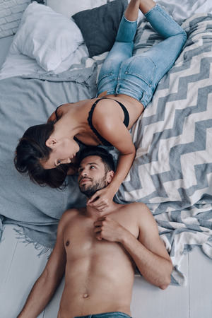 Simple joy of loving. Top view of beautiful young semi-dressed couple lying face to face while spending time in the bedroomの写真素材