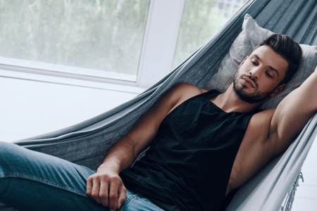 Dreaming. Top view of handsome young man in casual clothing sleeping while lying in the hammock indoorsの写真素材