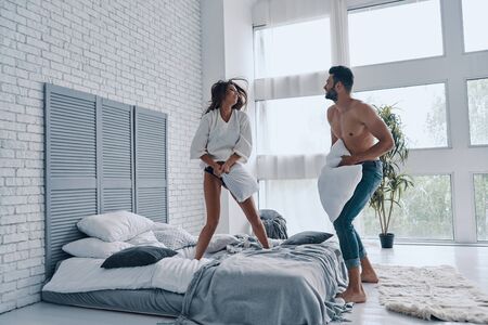 Crazy in love. Full length of happy young couple having a fun pillow fight while spending carefree time in the bedroomの写真素材