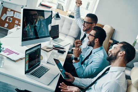 Great results! Group of young modern men in formalwear gesturing and smiling while working in the officeの写真素材