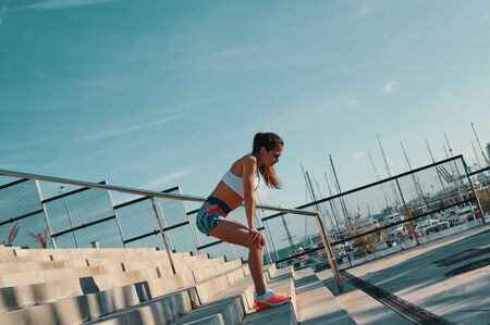 Healthy habits. Full length of beautiful young woman in sports clothing relaxing while exercising outdoorsの写真素材