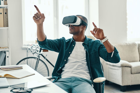 Cutting edge technologies. Handsome young African man wearing virtual reality simulator headset...