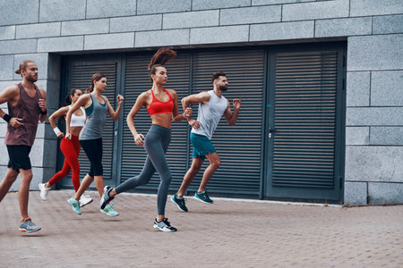 Group of young people in sports clothing jogging while exercising on the sidewalk outdoors