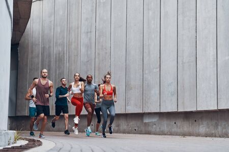 Full length of young people in sports clothing jogging while exercising outdoorsの写真素材