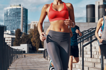 Close up of young woman in sports clothing jogging while exercising on the sidewalk outdoors