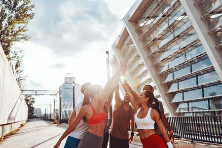 Group of young people in sports clothing holding hands together while standing outdoorsの写真素材